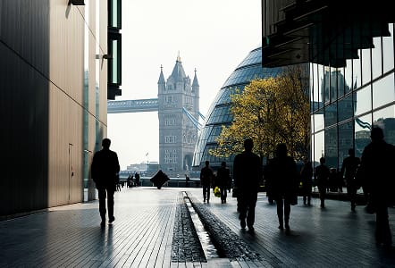 Silhouetted pedestrians walking near Tower Bridge and City Hall in London