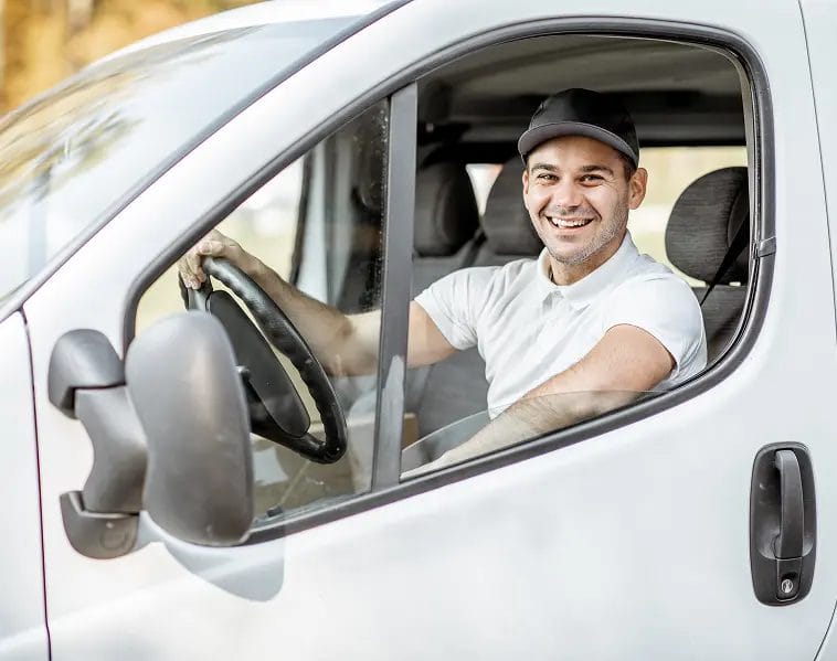 Smiling driver in a white polo shirt and cap behind the wheel of a van